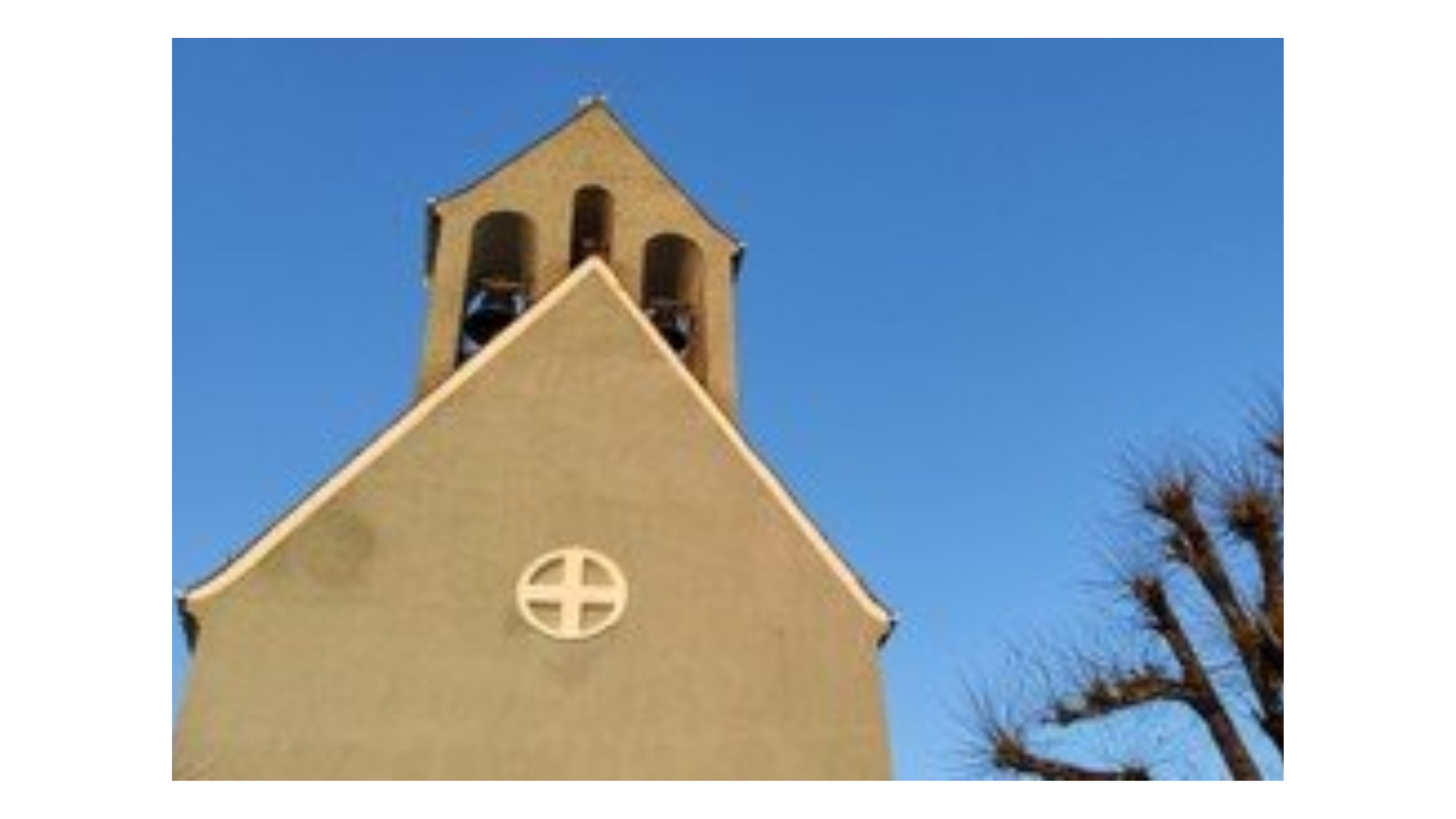 Kirchturm mit zwei Glocken und einem runden Kreuzsymbol an der Fassade.
