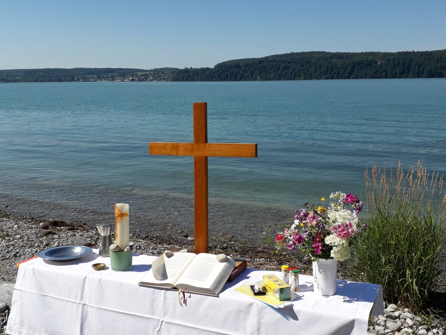 Altar mit Kreuz und Blumen am Ufer eines Sees.