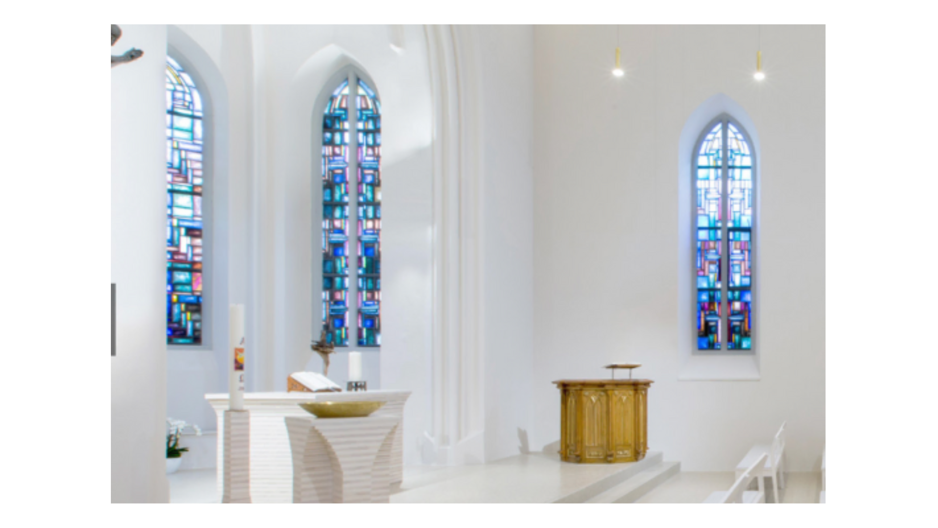 Heller Kircheninnenraum mit bunten Buntglasfenstern und einem modernen Altar.