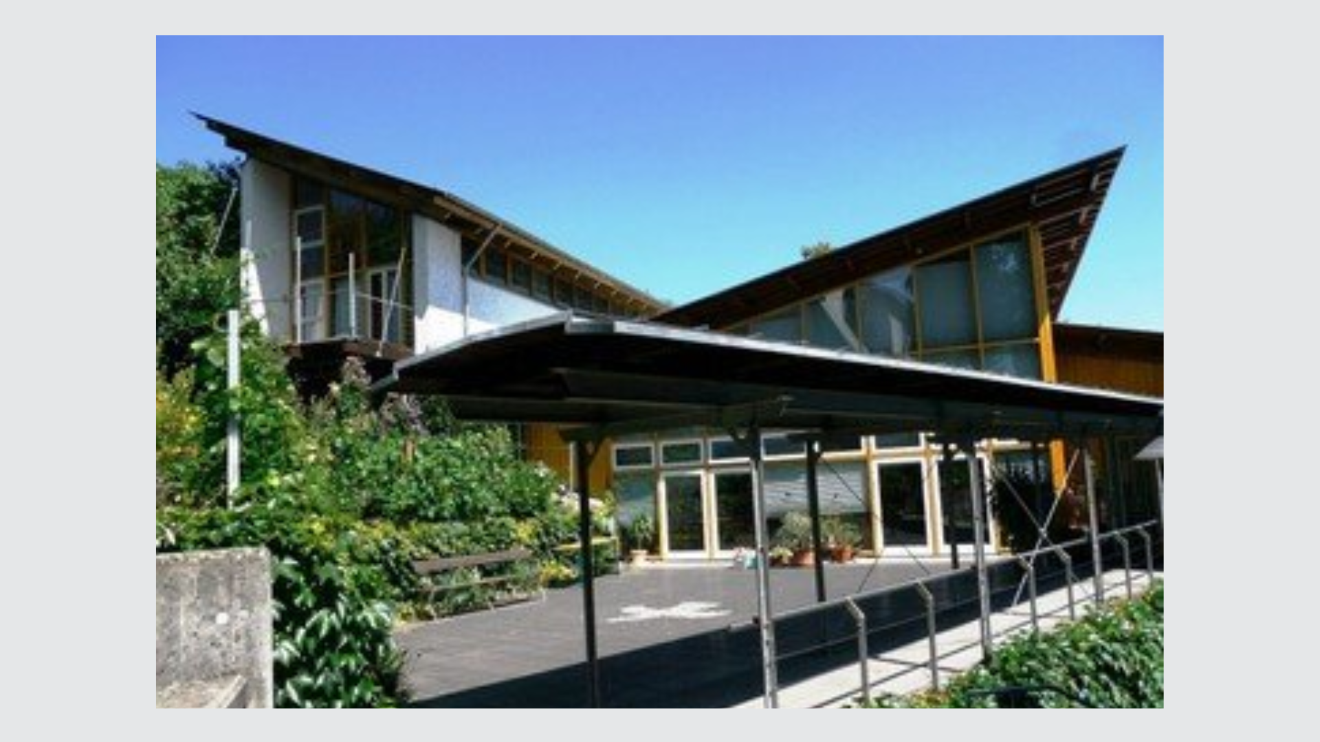 Modernes Gebäude mit auffälligem Dach und viel Glas, umgeben von Grün.