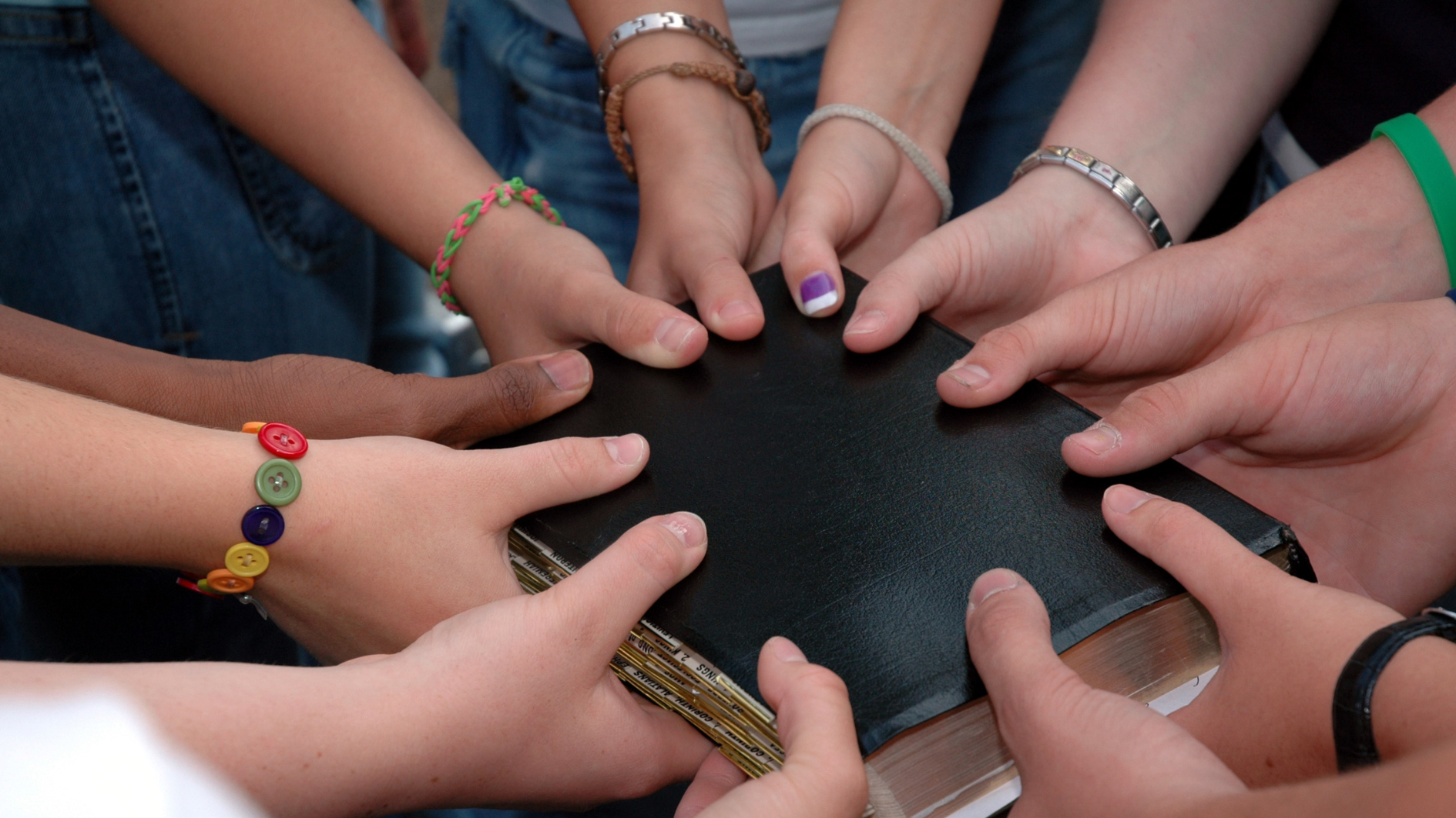 Mehrere Hände berühren eine schwarze Bibel.