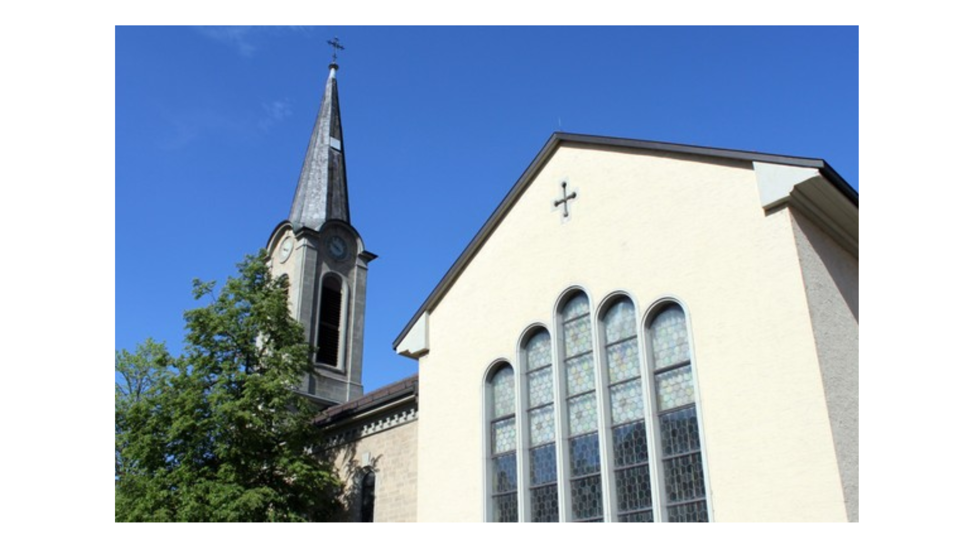 Eine Kirche mit spitzem Kirchturm und einem großen Fenster mit fünf Bögen.