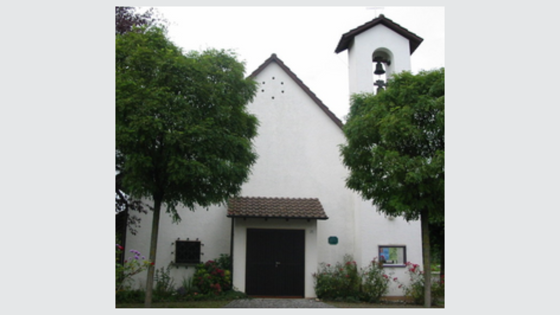 Eine weiße Kirche mit Glockenturm und zwei Bäumen davor.